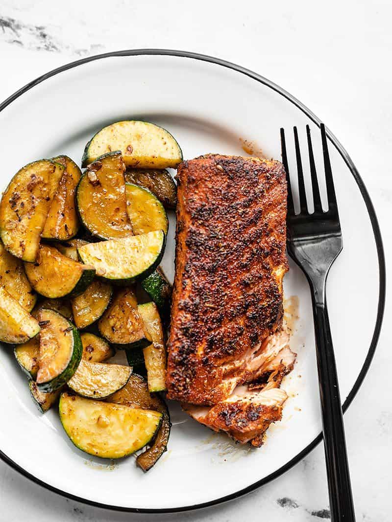 Blackened salmon with zucchini on a white plate with a black fork