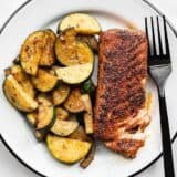 Blackened salmon with zucchini on a plate with a black fork on the side