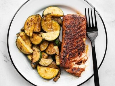 Blackened salmon with zucchini on a plate with a black fork on the side