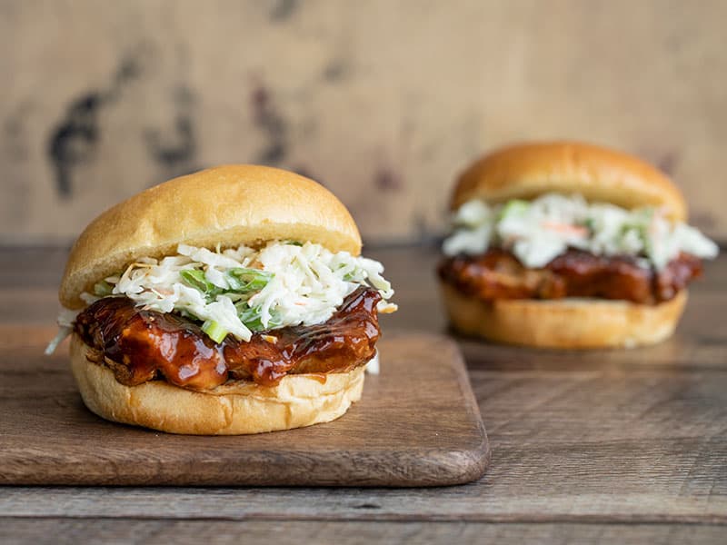 Two BBQ Chicken Sandwiches, one on a cutting board, the other in the background.