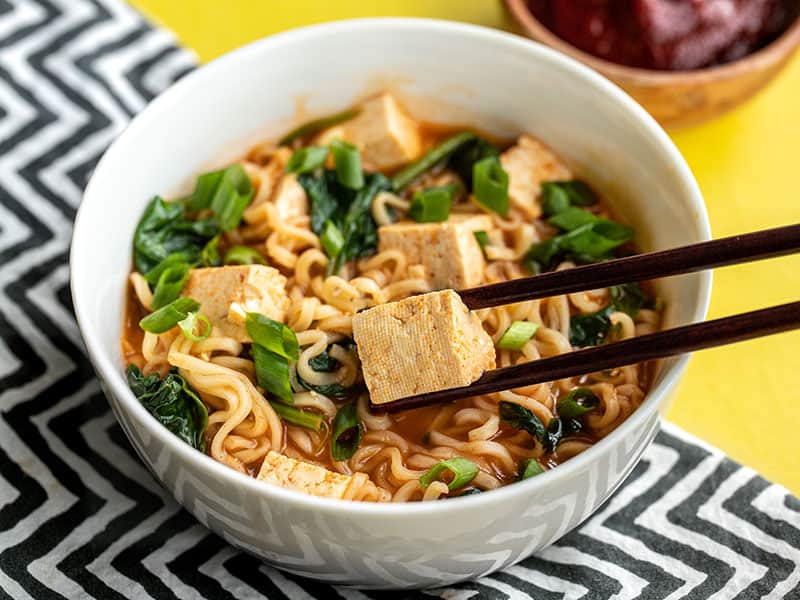 side view of a bowl of gochujang ramen with chopsticks picking up a piece of tofu