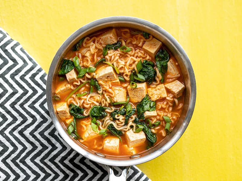 Gochujang ramen with tofu in the sauce pot on a yellow background with a black and white zig-zag napkin.