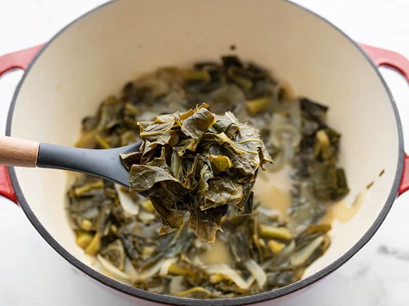 A spoon lifting some jerk seasoned collard greens out of the pot