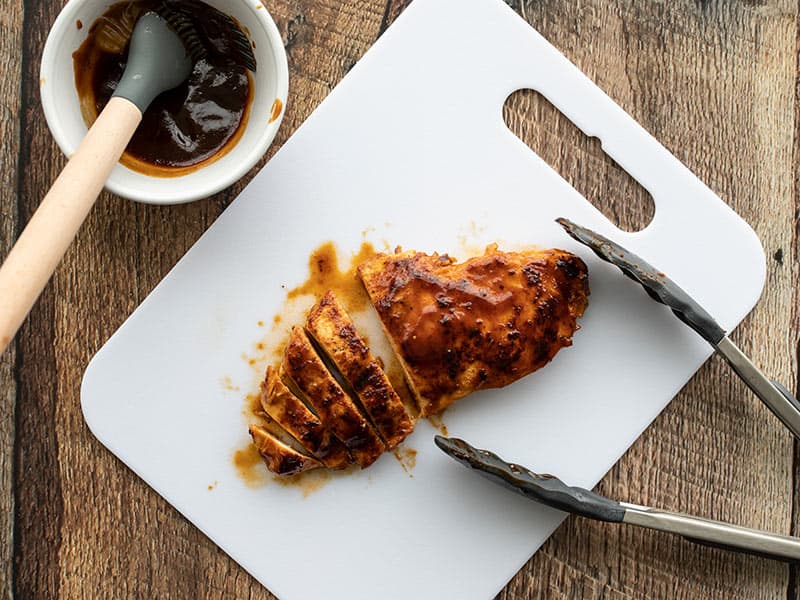 A Quick BBQ Chicken Breast on a cutting board with tongs, half sliced.