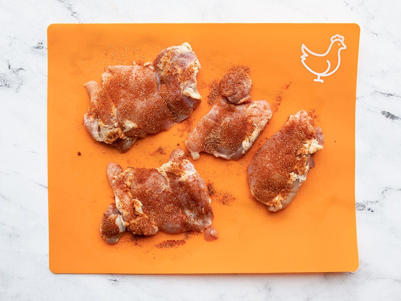 Seasoned chicken thighs on an orange cutting board