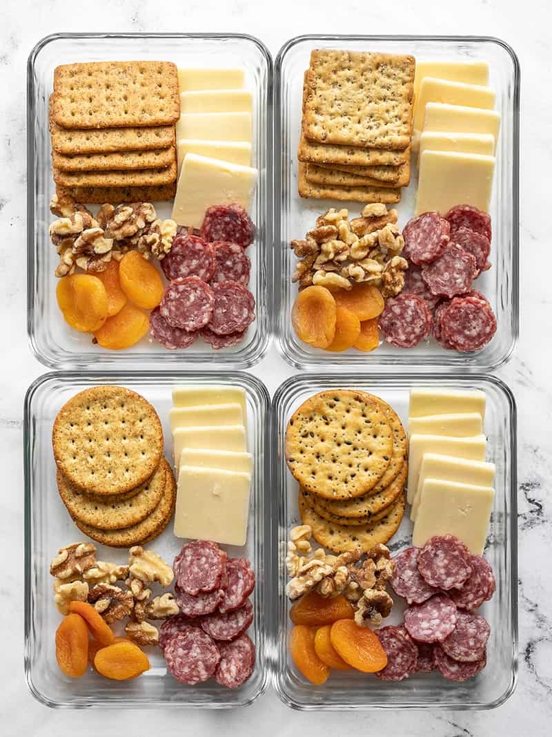 This easy no-cook lunch idea is perfect for the cheese lovers of the world! The Cheese Board Lunch Box makes a meal out of savory nibbles. Budgetbytes.com Four glass meal prep containers filled with the cheese board lunch box