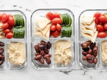 Three glass containers filled with hummus lunch box ingredients