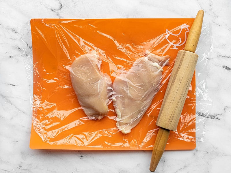 Pounded chicken breasts on a cutting board with a rolling pin