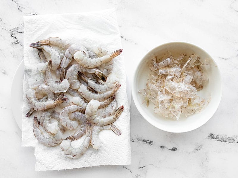 Peeled shrimp next to a bowl of shrimp peels