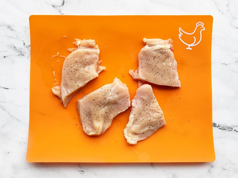 Chicken portions seasoned with salt and pepper on the cutting board