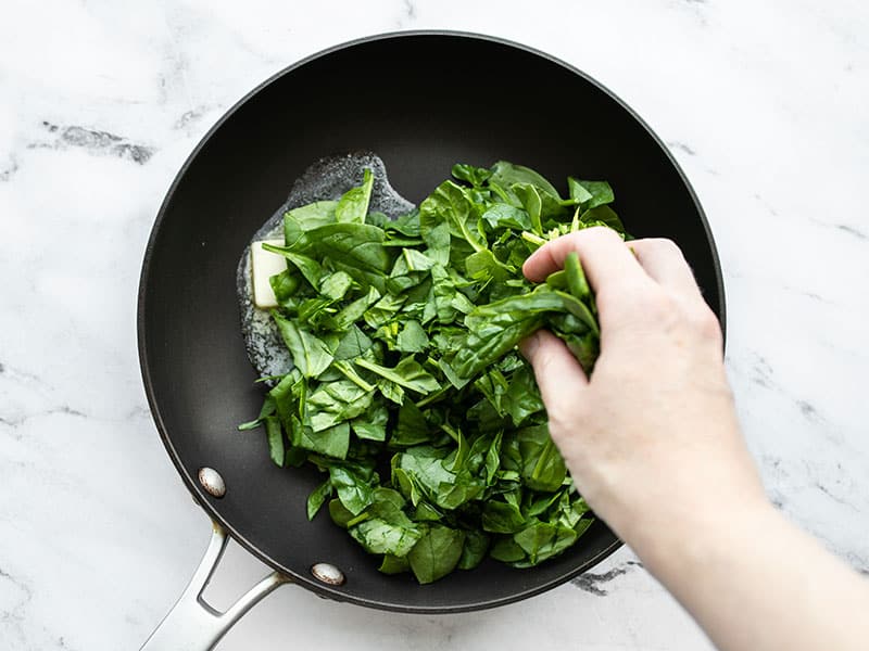 Spinach being added to a skillet with melted butter