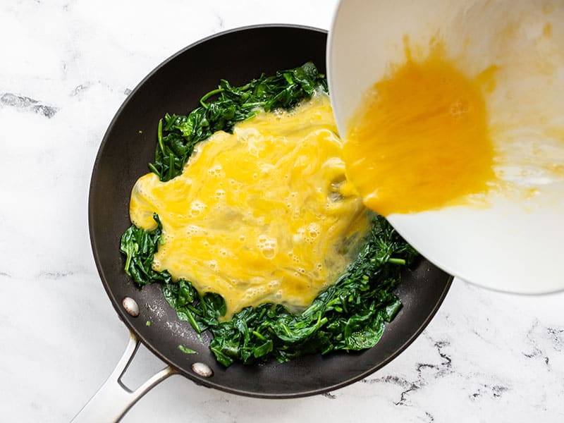 Whisked eggs being poured into the skillet with spinach
