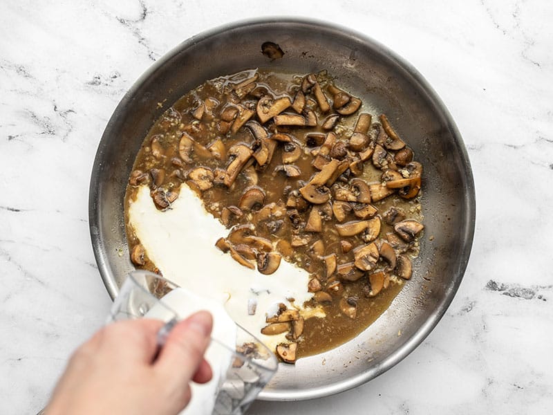 Cream being poured into the skillet with mushrooms