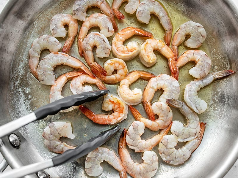 Shrimp in the skillet being flipped with tongs
