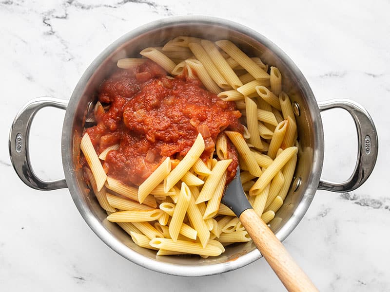 Stirring red sauce into cooked pasta.