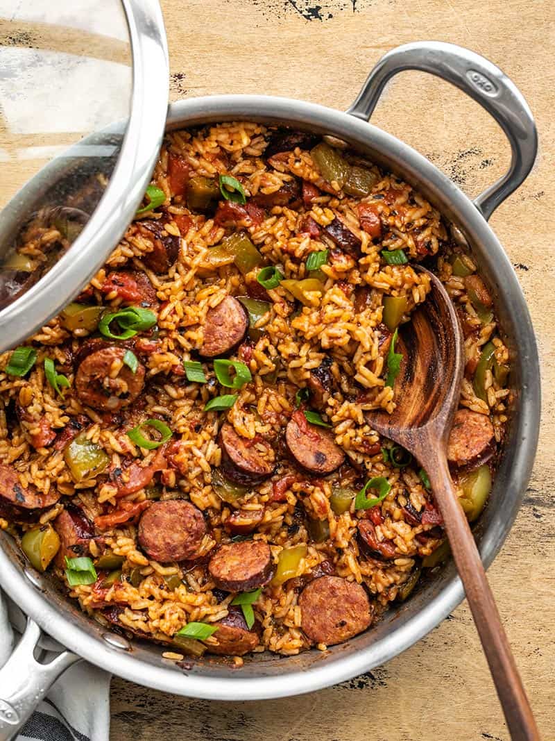 Cajun Sausage and Rice in the skillet with a wooden spoon and lid half on