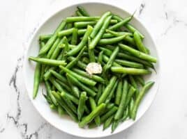 Overhead of a bowl of steamed green beans with butter, salt, and pepper.