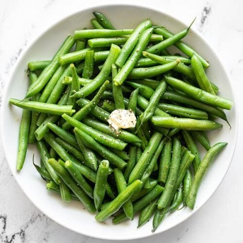 Overhead of a bowl of steamed green beans with butter, salt, and pepper.