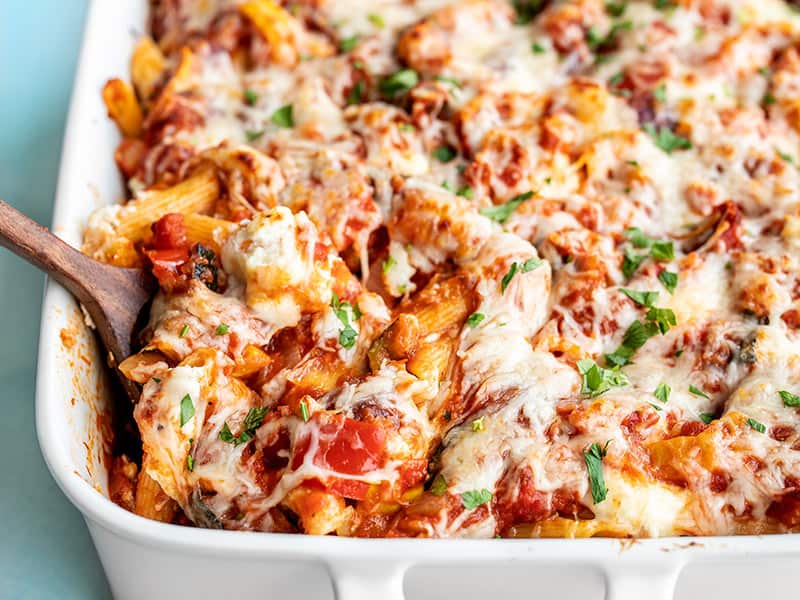 Close up front view of roasted vegetable baked penne being scooped out of the casserole dish