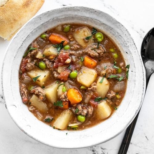 Overhead view of a bowl full of slow cooker hamburger stew with bread and a spoon on the side