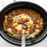 Slow cooker hamburger stew in a ladle over the slow cooker