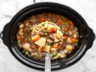 Slow cooker hamburger stew in a ladle over the slow cooker