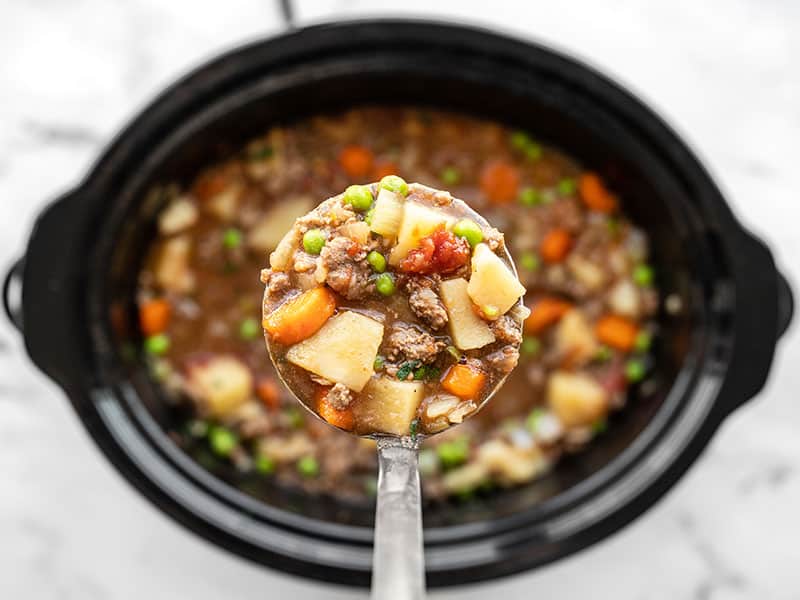 Slow cooker hamburger stew in a ladle over the slow cooker