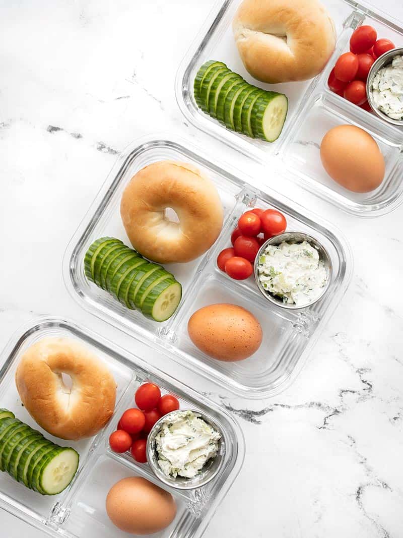 Three glass meal prep containers in a diagonal line filled with the bagel lunch box items