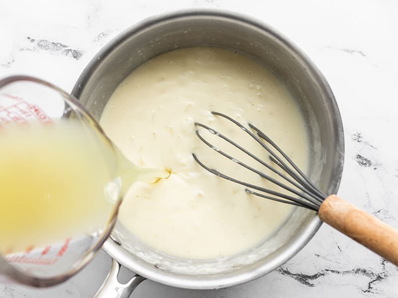 chicken broth being poured into the sauce pot