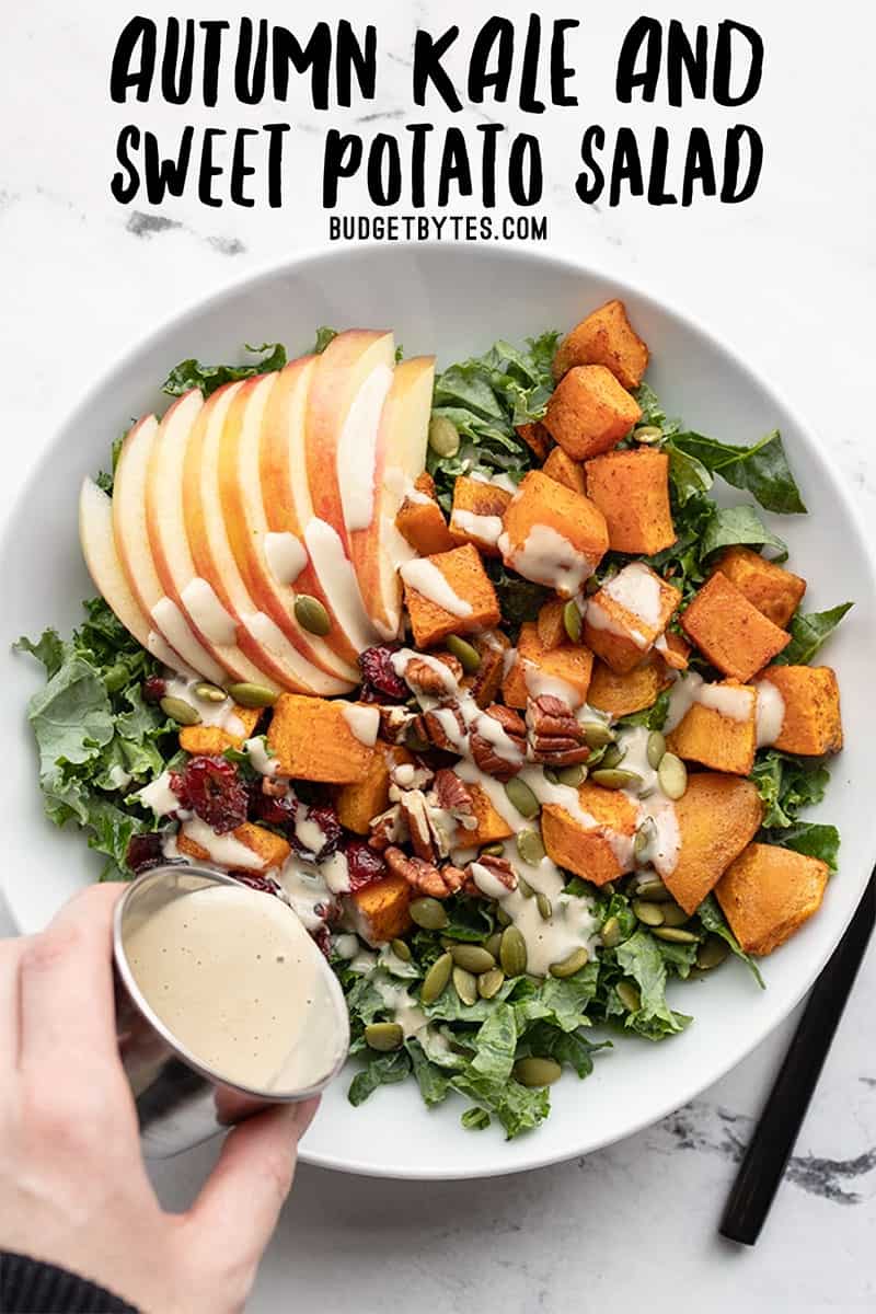 maple tahini dressing being poured over an autumn kale and sweet potato salad in a bowl