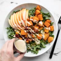 dressing being poured over the autumn kale and sweet potato salad in a bowl