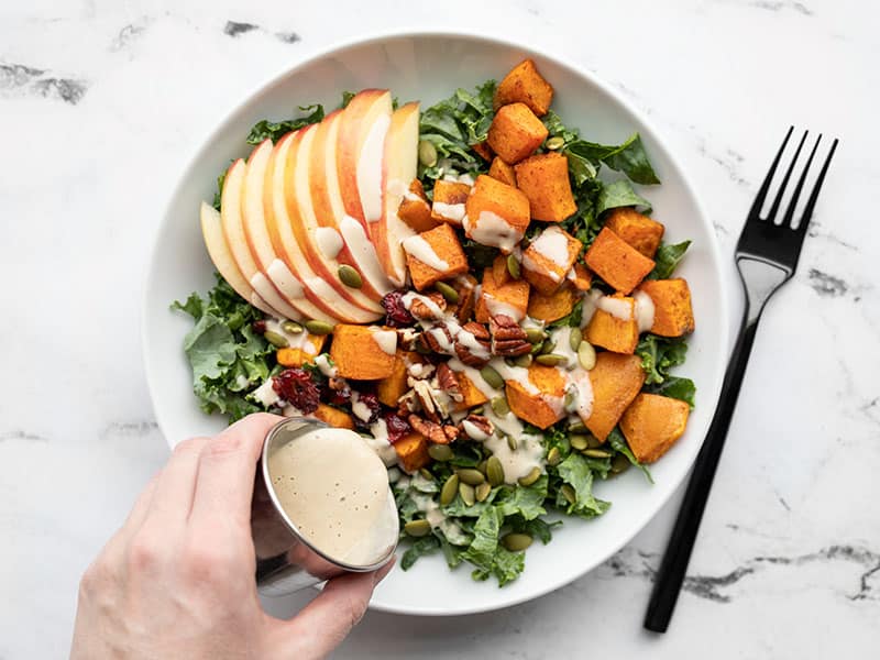 dressing being poured over the autumn kale and sweet potato salad in a bowl