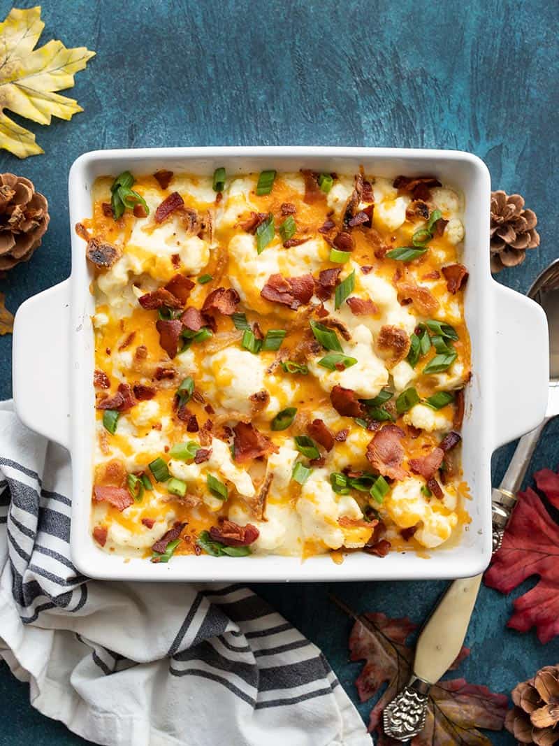 cheesy loaded cauliflower casserole on a blue background with a striped napkin