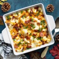 Overhead view of cheesy loaded cauliflower casserole on a blue background