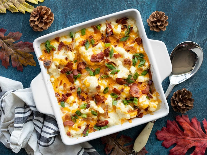 Overhead view of cheesy loaded cauliflower casserole on a blue background