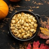 Overhead view of a bowl full of roasted pumpkin seeds on a wooden background.