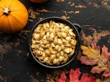 Overhead view of a bowl full of roasted pumpkin seeds on a wooden background.