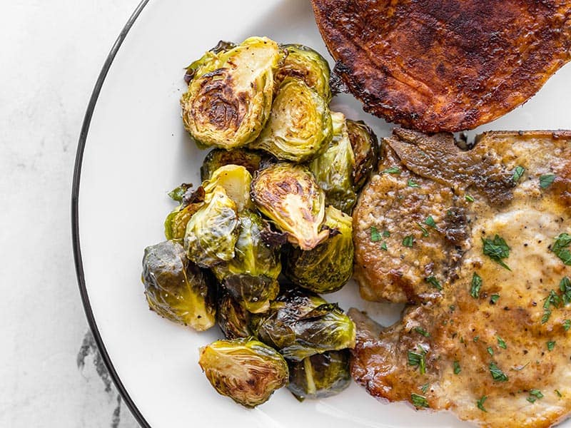 Roasted Brussels sprouts on a plate with pork chops and sweet potatoes