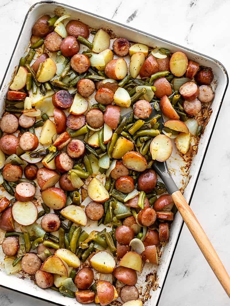 Sheet pan kielbasa, potatoes, and green beans with a spatula