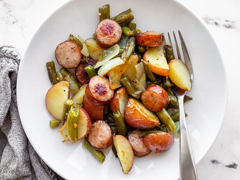 Sheet pan kielbasa, potatoes, and green beans in a bowl with a fork