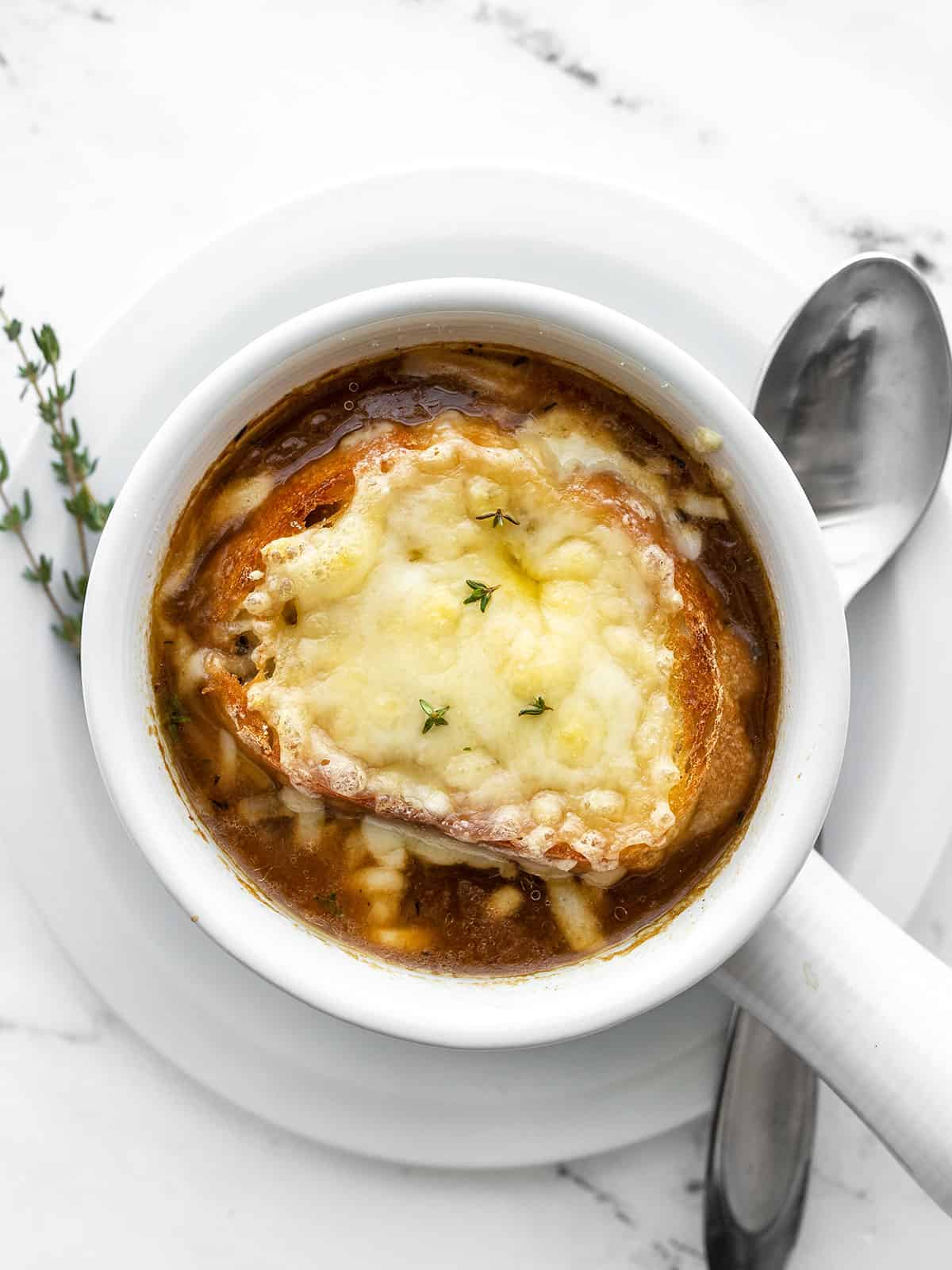 One bowl of french onion soup garnished with fresh thyme, spoon on the side