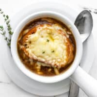 Overhead view of one bowl of french onion soup with a spoon and fresh thyme on the side