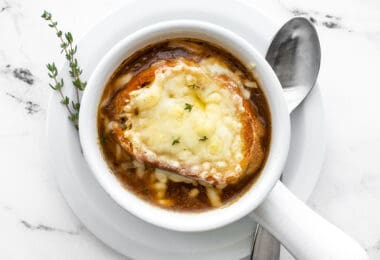 Overhead view of one bowl of french onion soup with a spoon and fresh thyme on the side