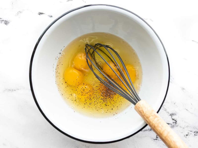 Eggs in a bowl with salt, pepper, and a whisk