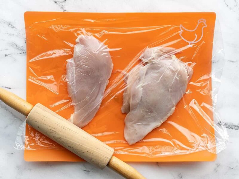 Chicken breast on a cutting board being pounded with a rolling pin