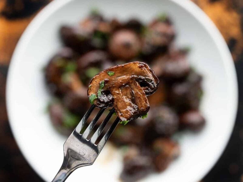 Close up view of a balsamic roasted mushroom on a fork with the bowl in the background