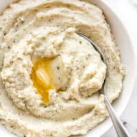 Garlic Herb Mashed Cauliflower in a bowl with a spoon and melted butter