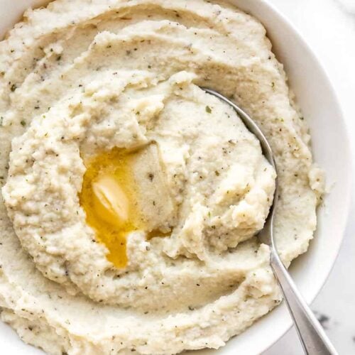 Garlic Herb Mashed Cauliflower in a bowl with a spoon and melted butter