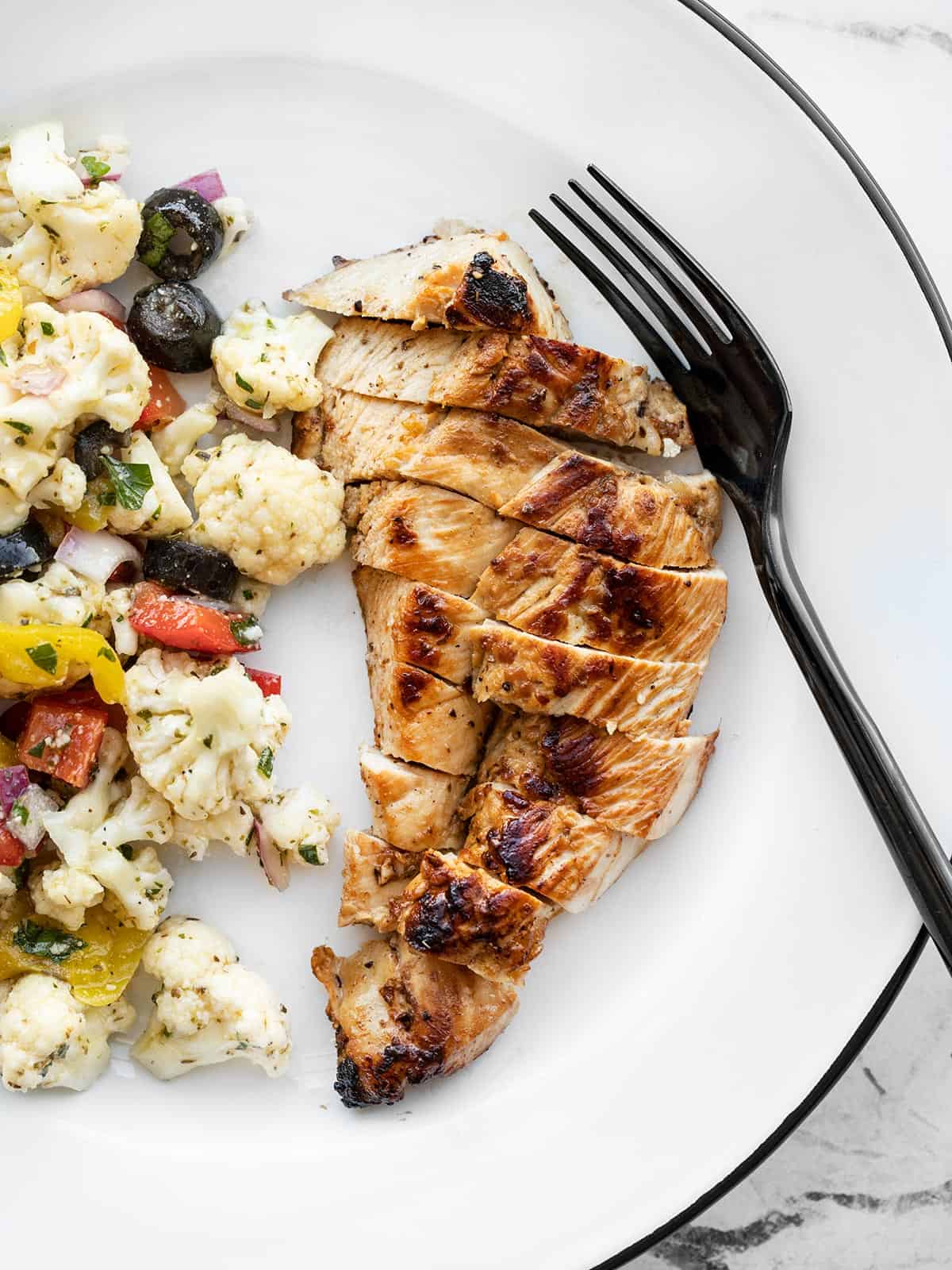 Sliced garlic marinated chicken on a plate with a fork and cauliflower salad