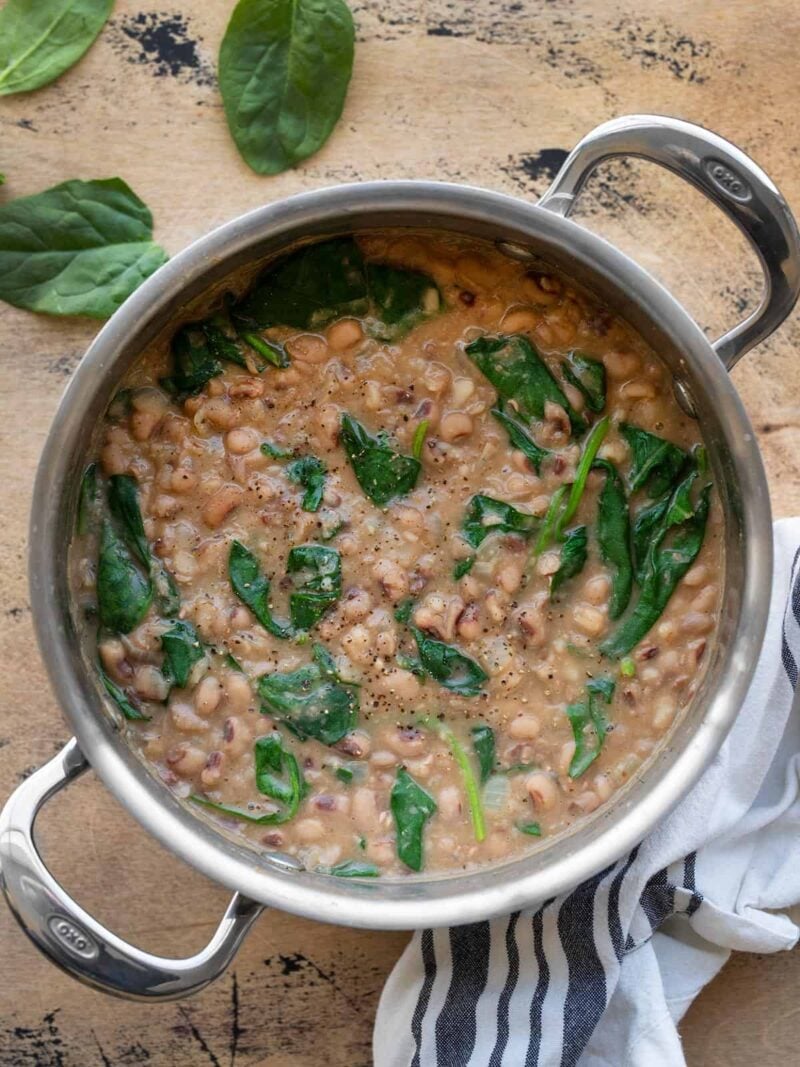 Overhead view of a pot of black eyed peas and greens on a wooden surface